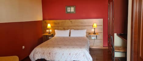 Habitación de hotel con cabecera de madera, dos mesitas de noche con lámparas, cama con ropa de cama floral y una pared de acento roja.