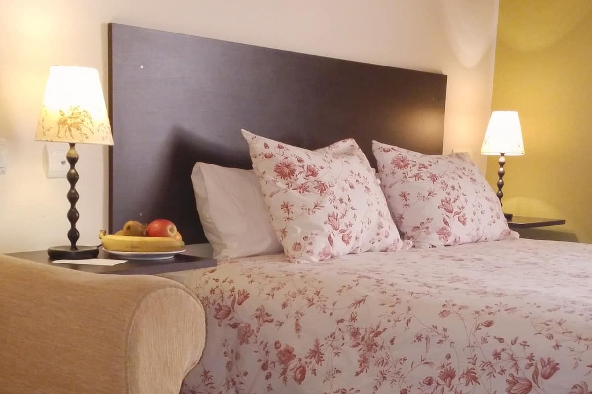 Ein Hotelzimmer mit einem Bett, zwei Nachttischen, einem kleinen Tisch, einem gerahmten Bild an der Wand und einem Teller mit Dessert auf dem Tisch.