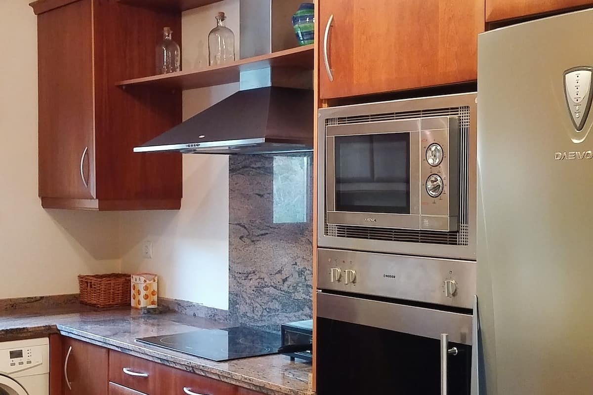 Eine Küche mit Holzausstattung, einem Edelstahlkühlschrank, einem Einbauofen und einer Mikrowelle.