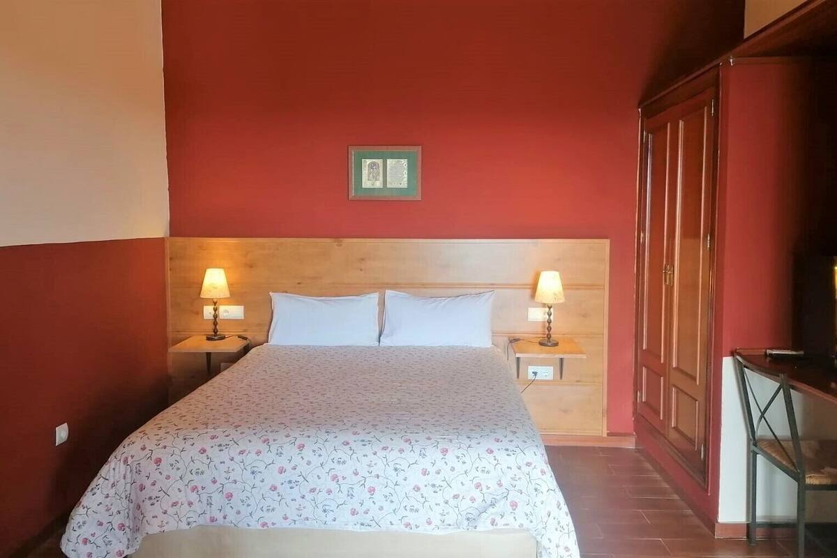 Ein Hotelzimmer mit einem hölzernen Kopfteil, einem Bett mit floralem Bettbezug, zwei Nachttischlampen und einem Holzschrank.