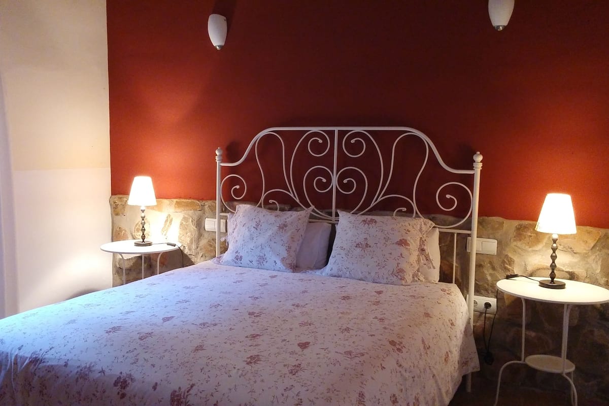 Ein Bett mit floralem Überwurf, zwei Nachttische mit Lampen sowie eine Wand mit Steinverkleidung.