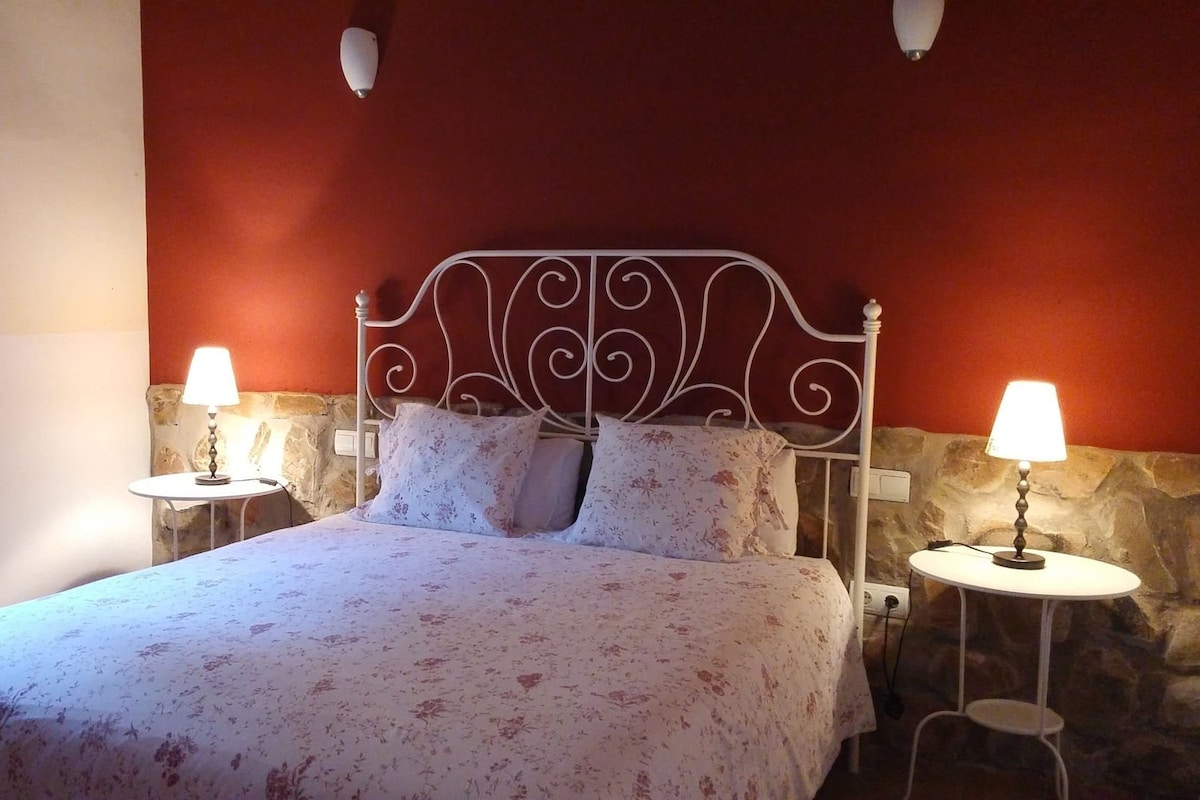 A bed with a floral bedspread, two bedside lamps, and a stone wall.