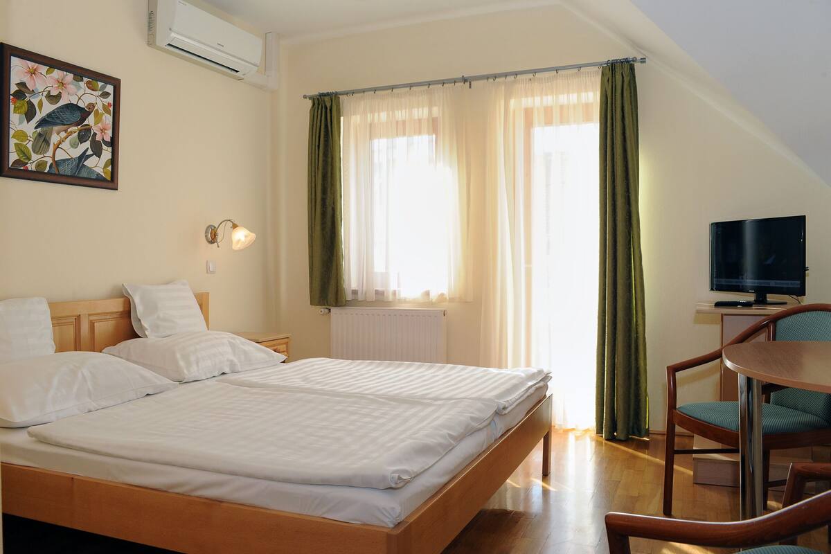 A hotel room with two beds, a desk with a chair, a television, and a window with curtains.