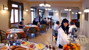 Uma área de refeições com mesas preparadas para o café da manhã, incluindo pão, doces, frutas e bebidas.
