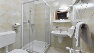 Un baño con ducha envuelta en cristal, inodoro, lavamanos y toallero.