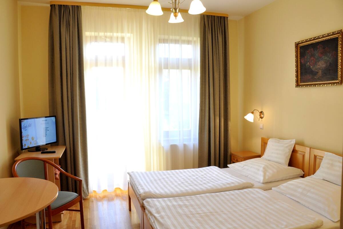 A hotel room with two beds, a desk with a computer, a chair, and a painting on the wall.