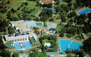 An aerial view of a resort with multiple swimming pools, tennis courts, and lush green surroundings.