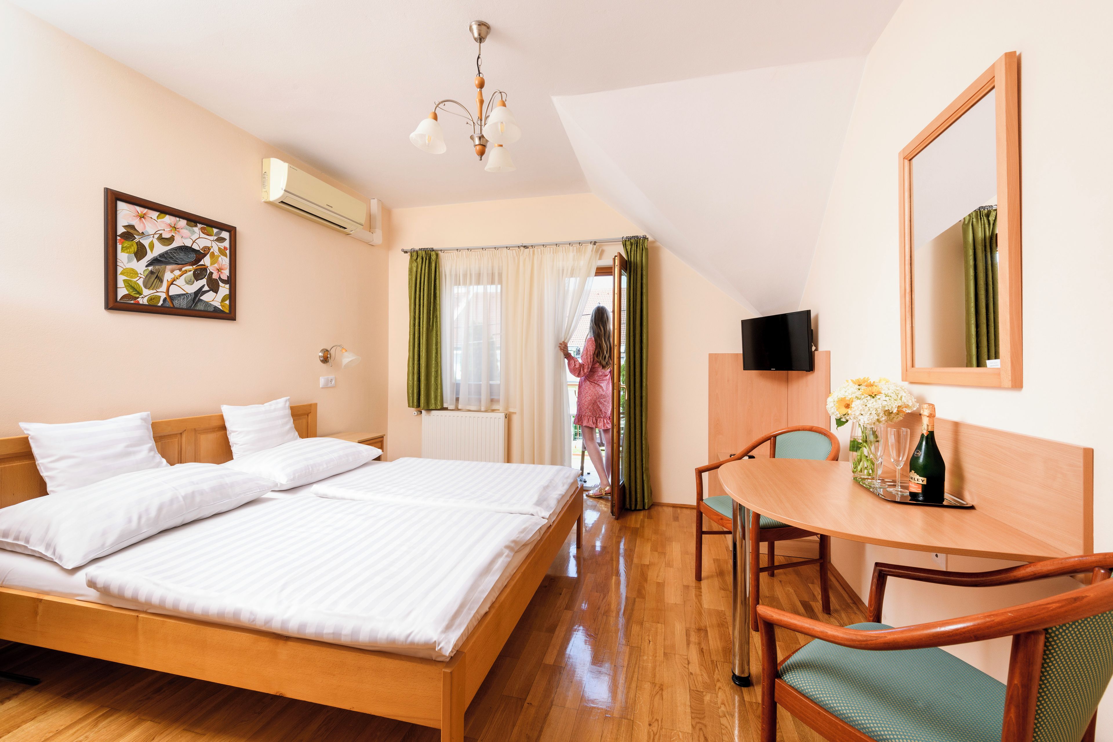 A hotel room with a bed, a desk with a chair, a television, and a window with curtains.