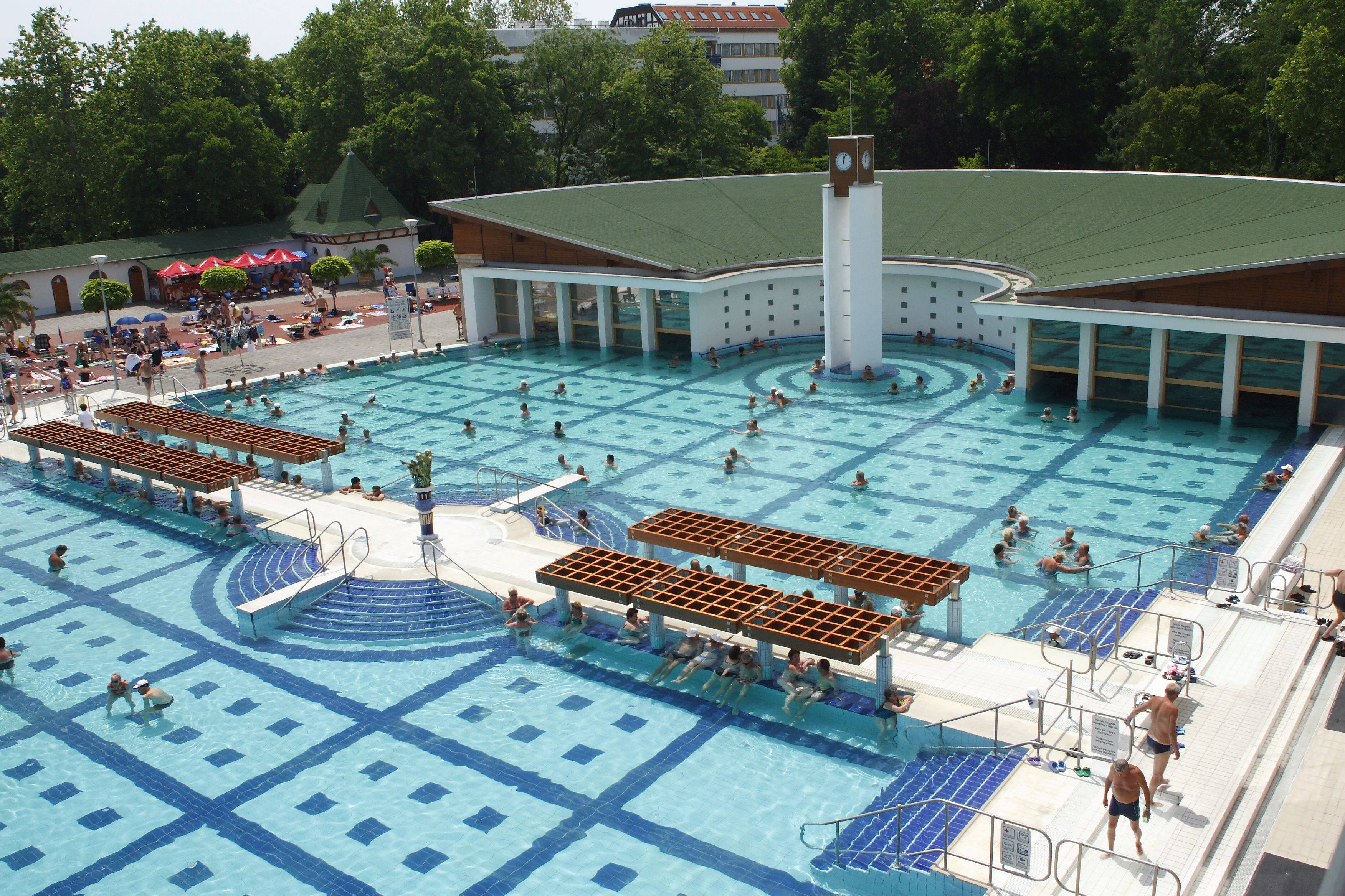 Una amplia piscina exterior con varias pistas de natación, rodeada por una zona cubierta con asientos.
