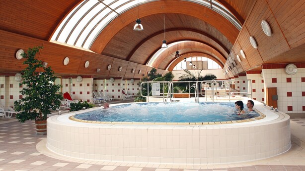 Uma grande piscina interior com teto de madeira e paredes azulejadas.