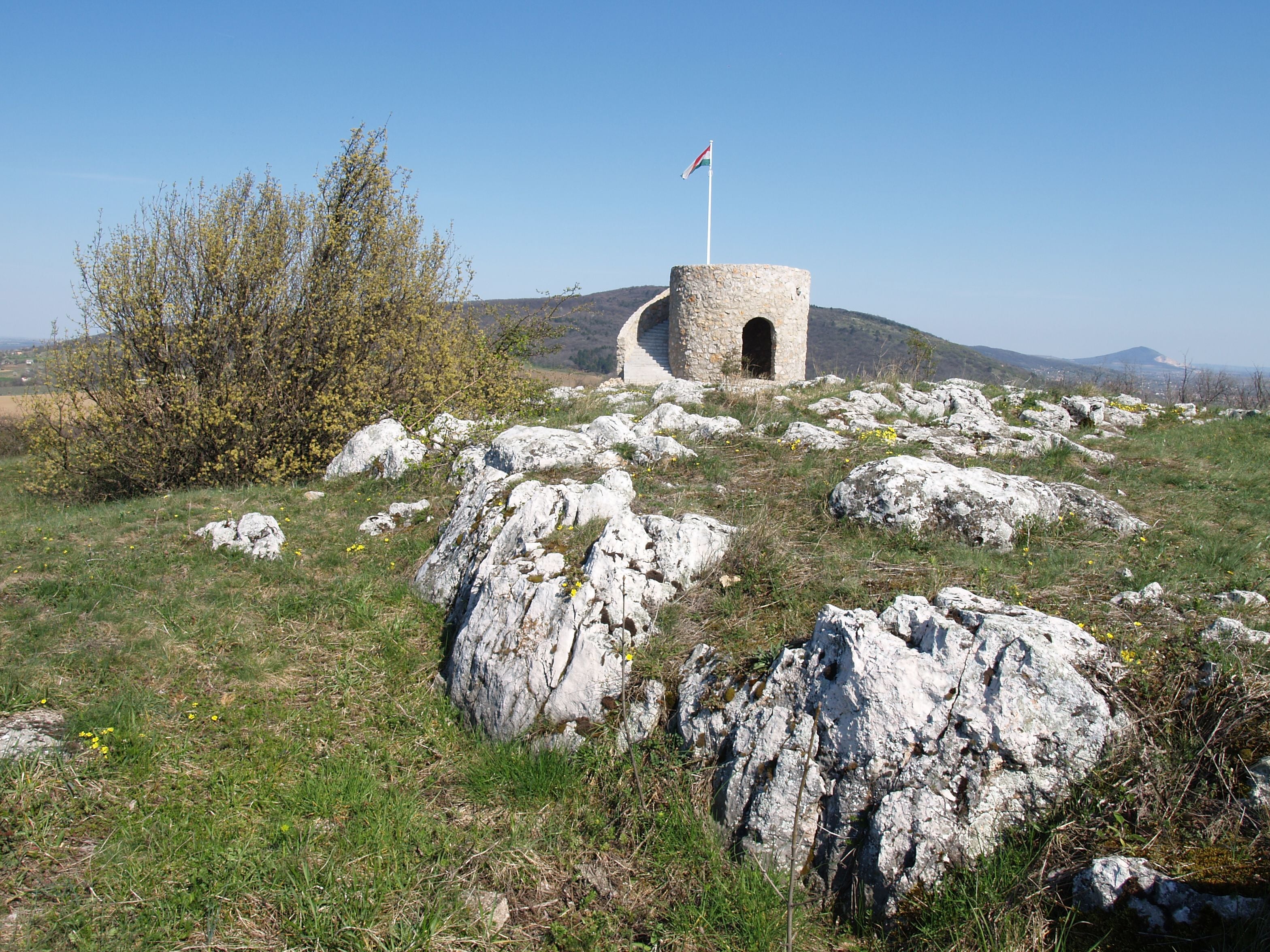 A stone structure with a flag on top, surrounded by rocks and sparse vegetation.