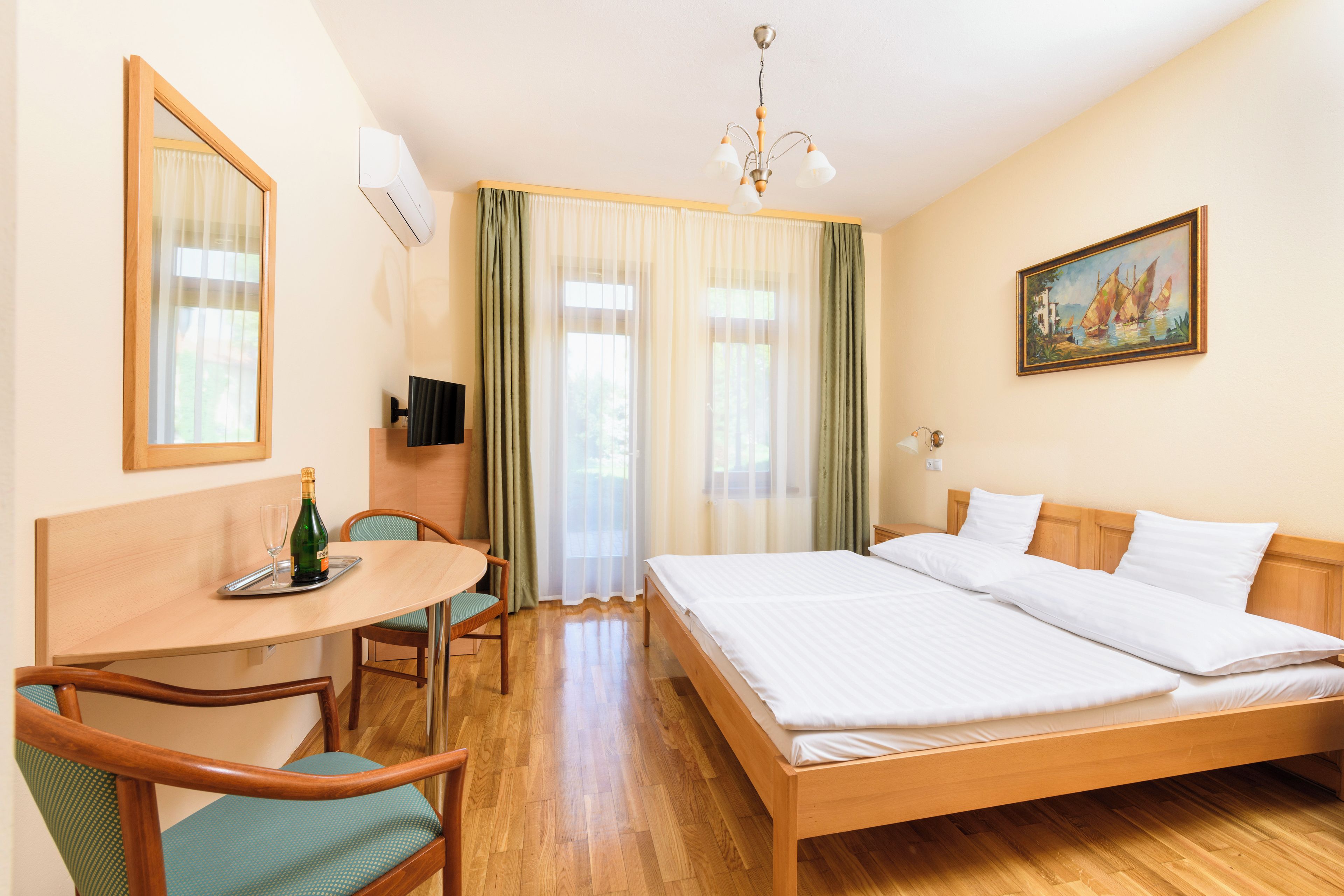 A hotel room with a wooden bed, a desk with a chair, a television, and a painting on the wall.