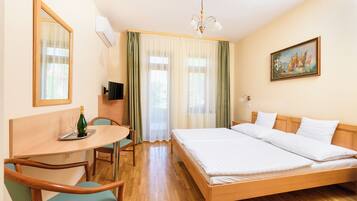 A hotel room with a wooden bed, a desk with a chair, a television, and a painting on the wall.