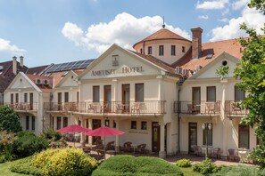 A hotel with a central building and two side wings, featuring outdoor seating and a garden. - Ametiszt Hotel Harkany (Harkany)