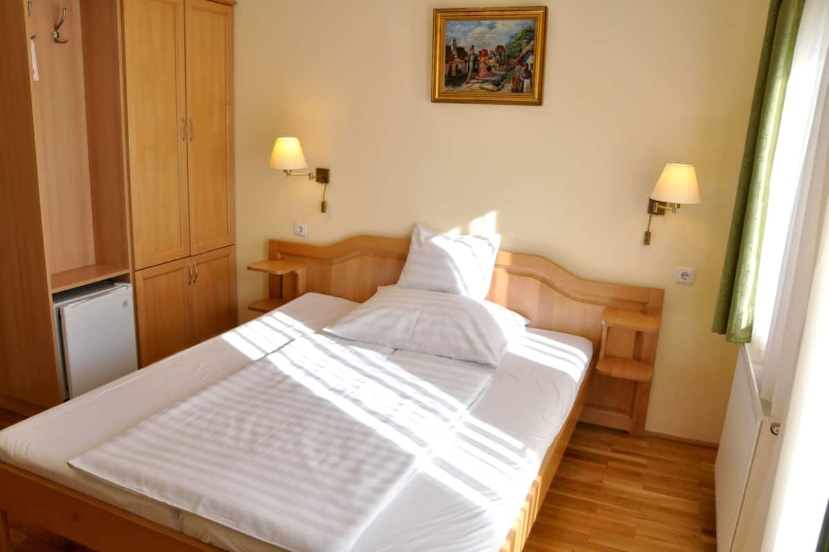 A neatly made bed with white linens, two bedside lamps, and a painting on the wall.
