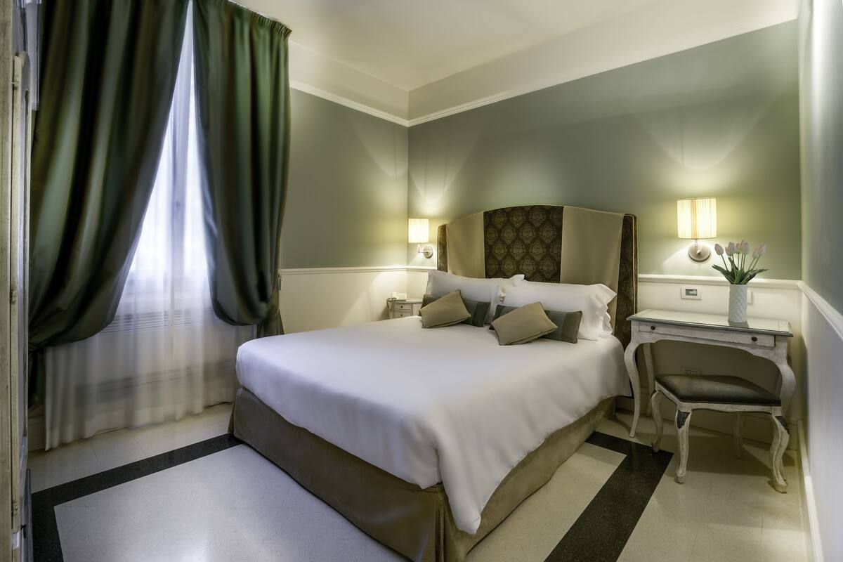 Une chambre d’hôtel avec un grand lit, des lampes de chevet, un bureau avec une chaise et une fenêtre avec des rideaux.