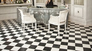 Un comptoir d’accueil avec un sol à carreaux noirs et blancs, un lustre et une réceptionniste.