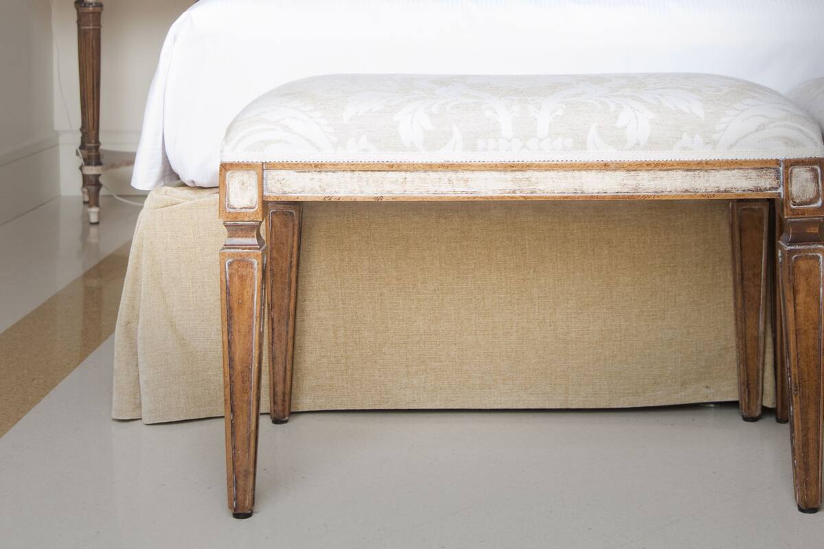 Un lit bien fait, avec une tête de lit, une table de chevet avec une lampe et un banc au pied du lit.