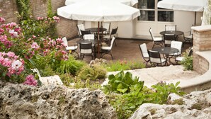 Un espace extérieur aménagé en terrasse, avec des parasols blancs, des chaises noires et un mur en briques.