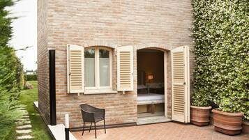 Una casa de ladrillo de dos pisos con un patio, un pequeño jardín y un dormitorio visible con una cama y una mesita de noche.