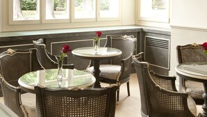 Un espace repas avec des tables rondes et des chaises en osier, de grandes fenêtres donnant sur la verdure et un plafond blanc.