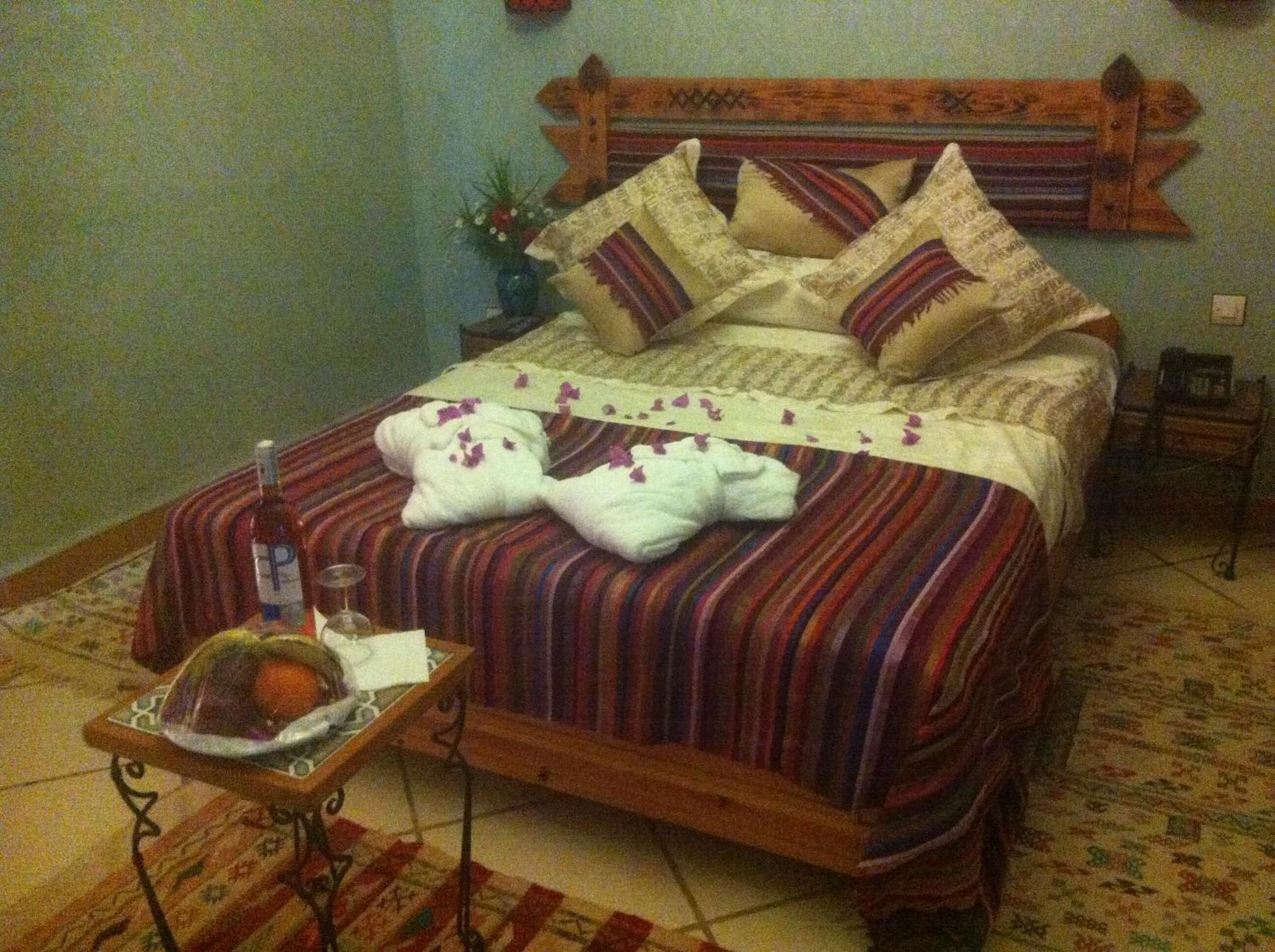 Una cama con cabecera de madera, ropa de cama a rayas y dos toallas blancas con flores púrpuras.