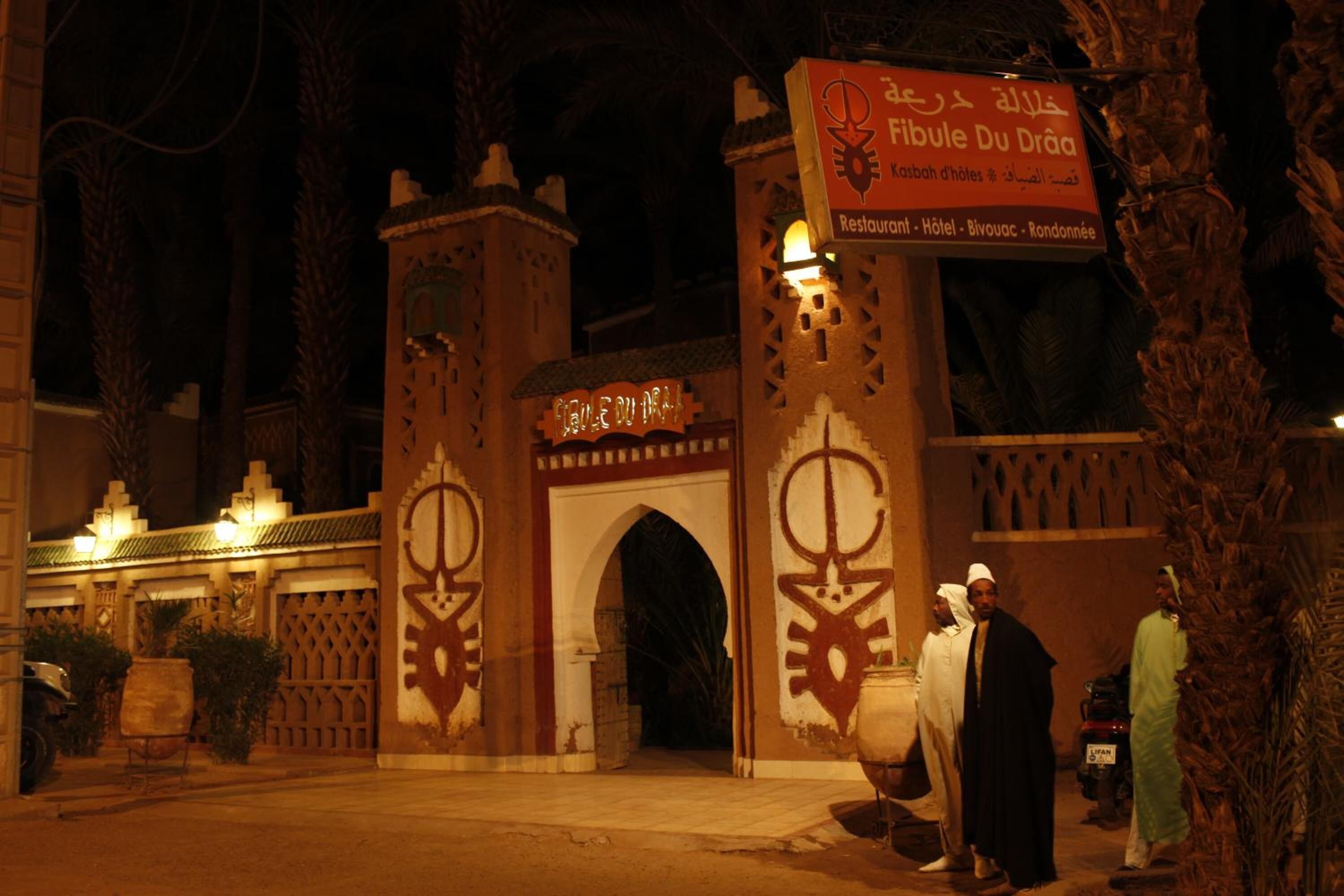 A traditional building with a sign reading "Fibule Du Drâa" and a restaurant/hotel/hotel sign.