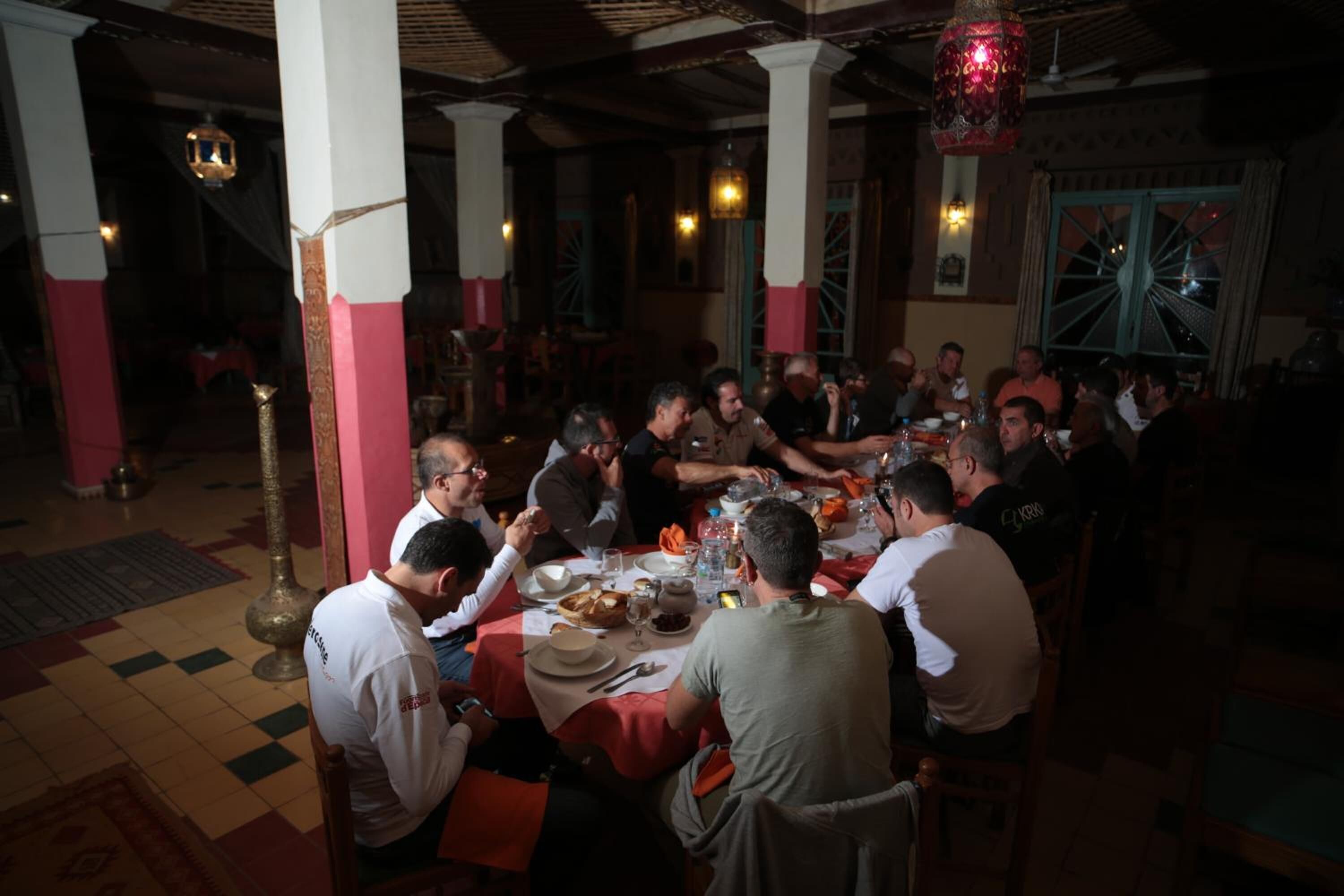 Eine Gruppe von Personen speist in einem Restaurant mit traditioneller Einrichtung, das Säulen und hängende Laternen aufweist.
