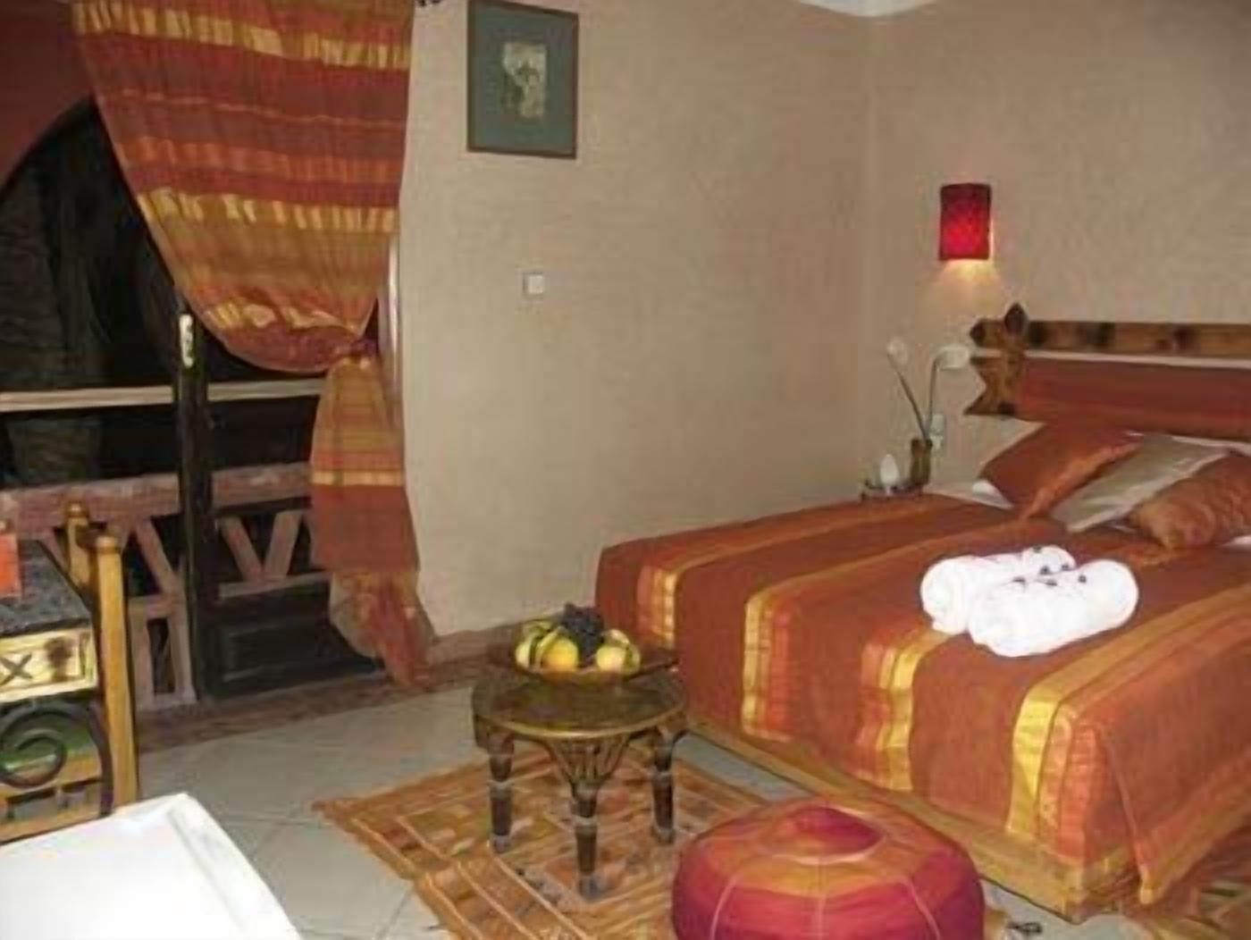 A room with a bed, a small table, a chair, and a wall-mounted light.