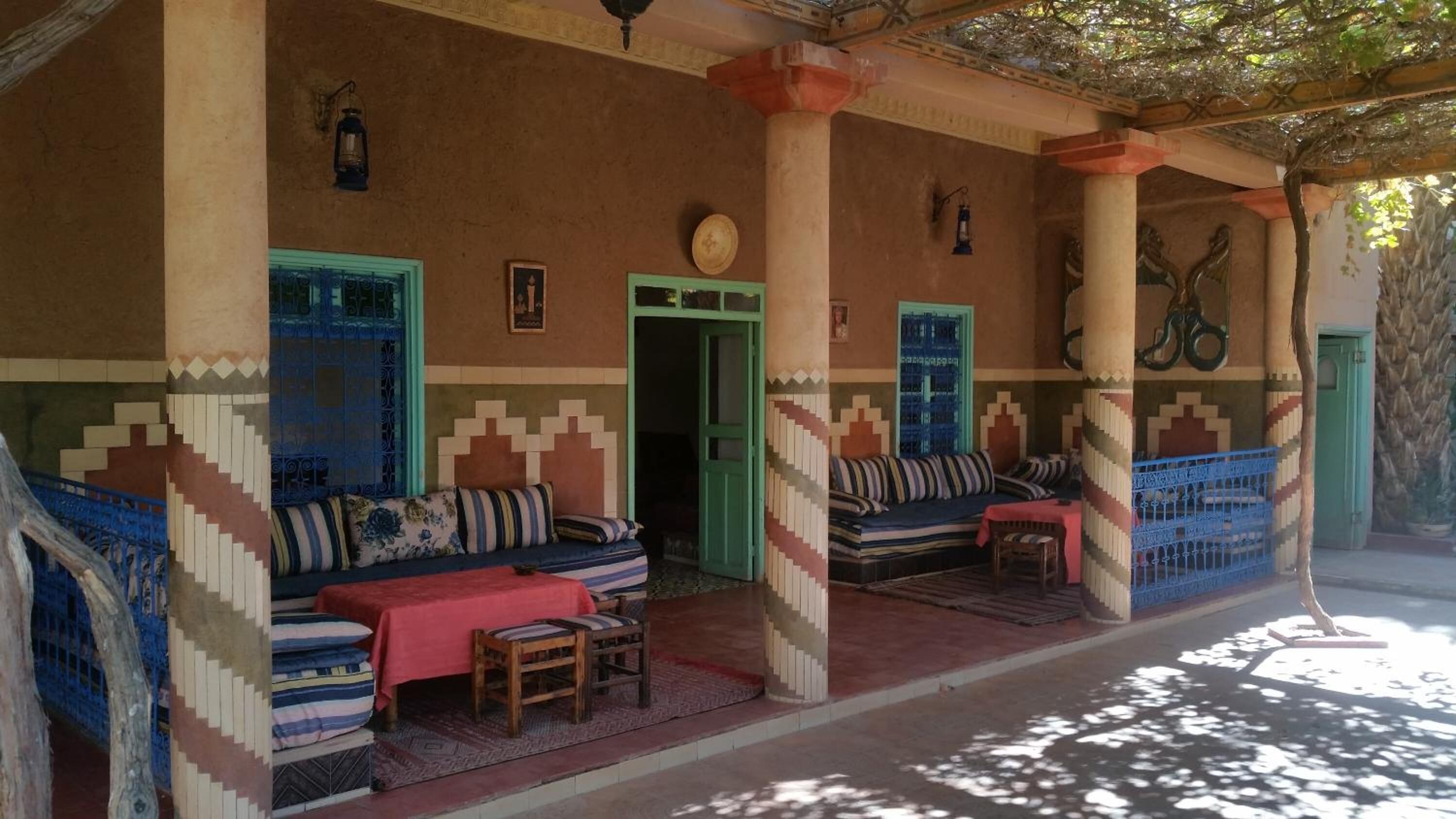 Un área de estar al aire libre techada con cojines estampados y una pequeña mesa, columnas y puertas con diseños geométricos.