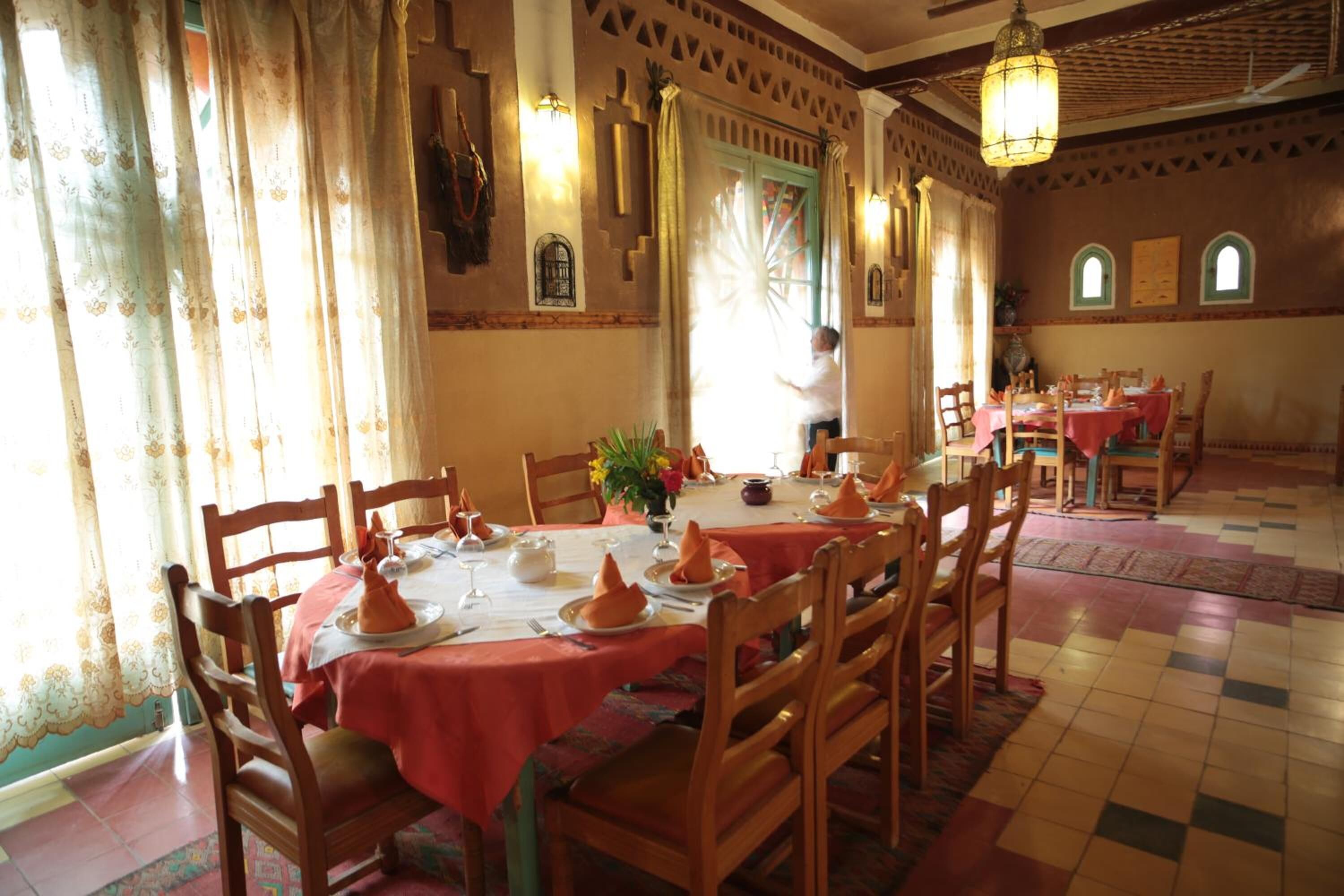 A dining area with tables set for a meal, featuring traditional tablecloths and wooden chairs.