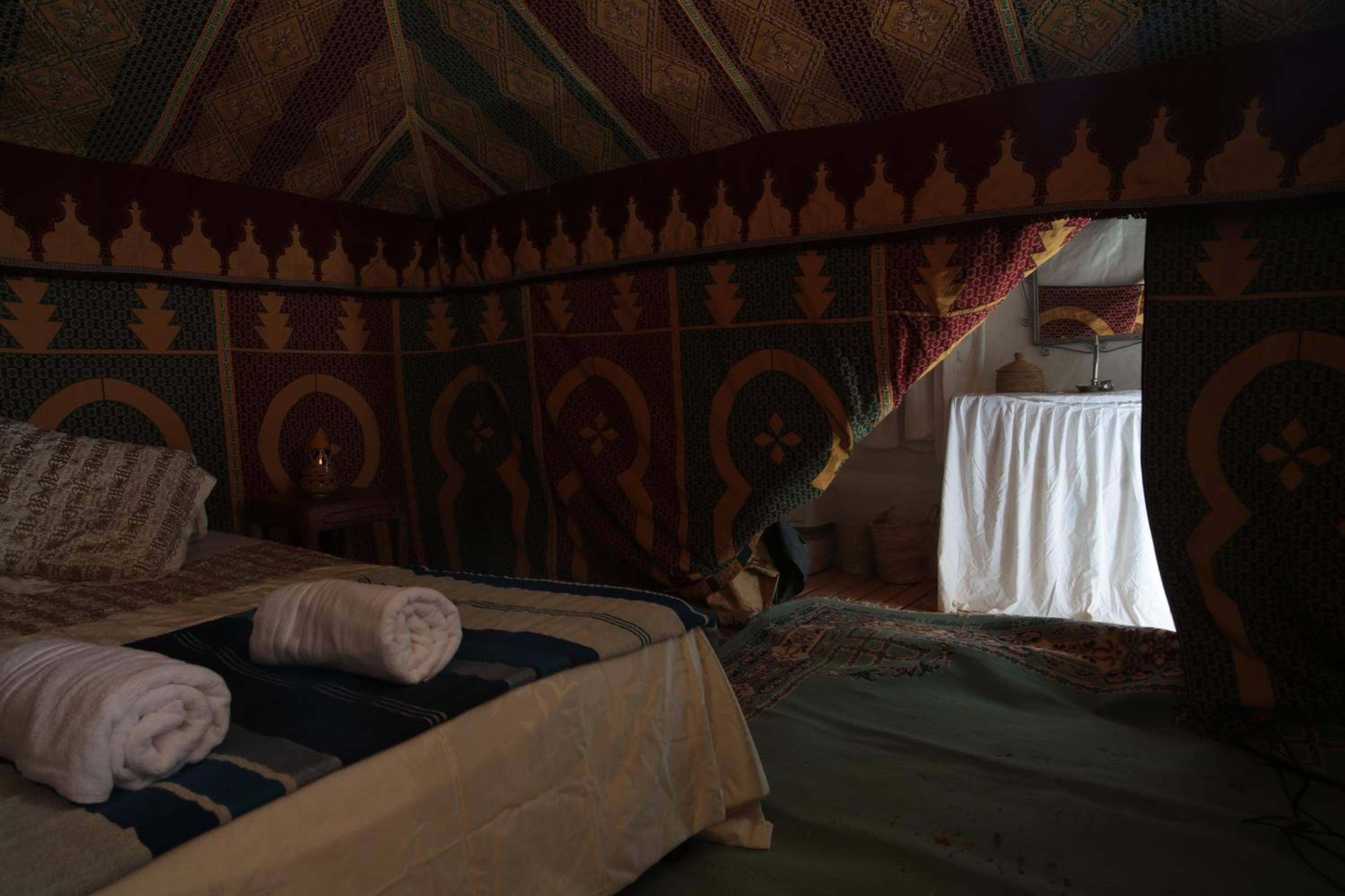 A room with a patterned ceiling, a bed with a white cover, and a table with a white tablecloth.