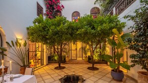A courtyard with a tiled floor, potted plants, a central fountain, and a table set for dining. - Riad Alma (Marrakech)