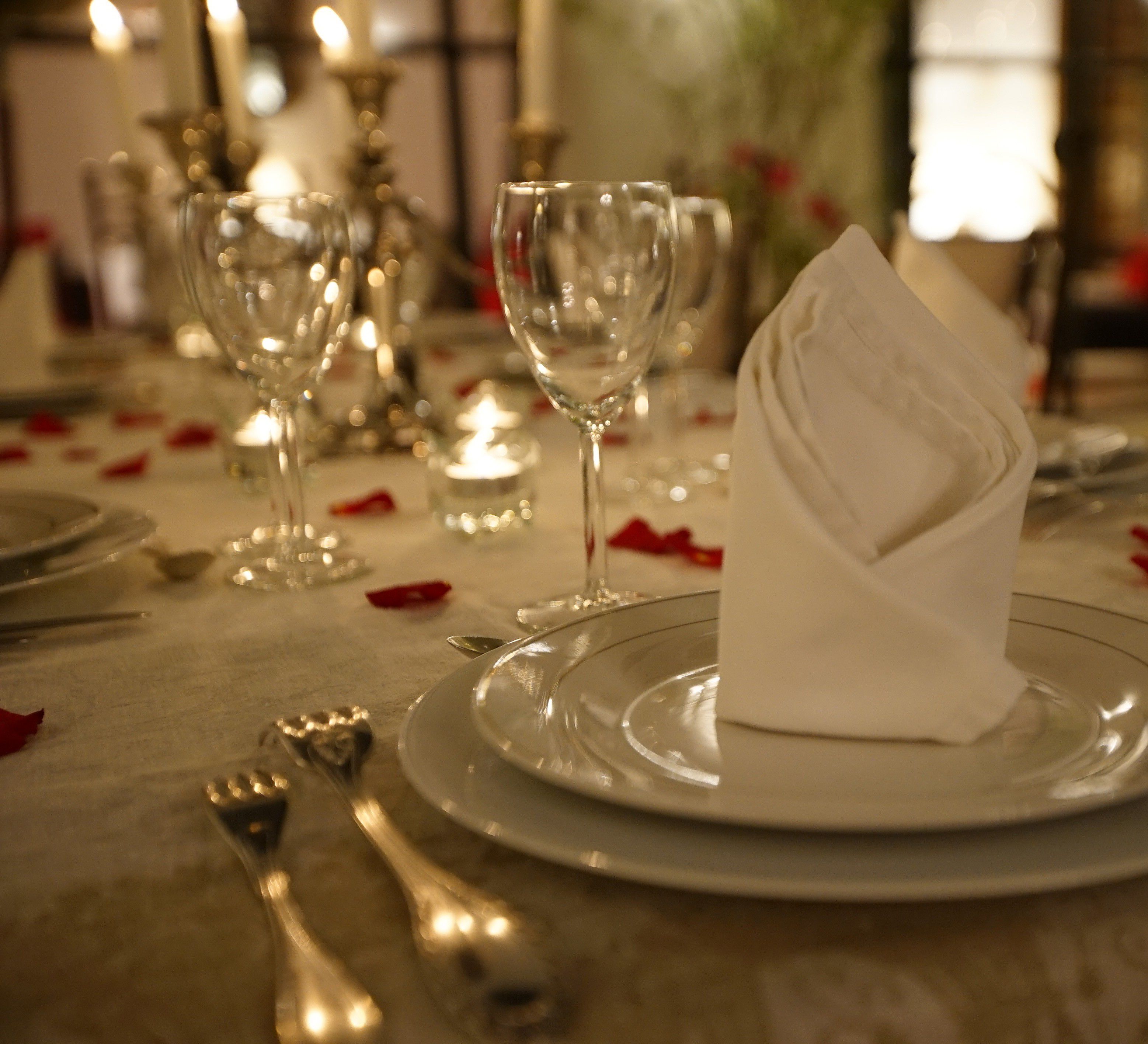 Une table dressée pour un dîner formel, avec de la vaisselle transparente, une serviette pliée et une bougie allumée.