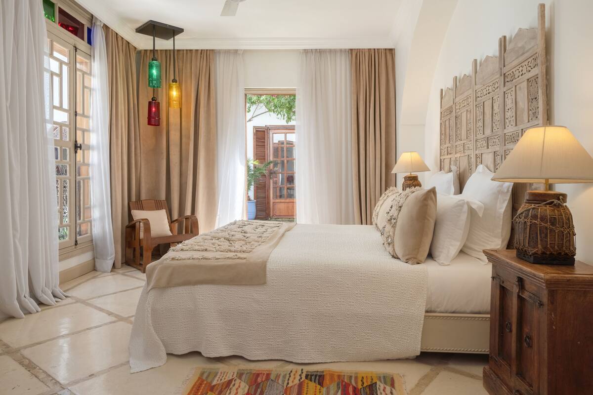 Quarto com cama grande, duas luminárias de cabeceira, cabeceira de madeira e vista para o exterior.