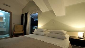 A bedroom with a bed, pillows, a chair, a nightstand, and a bathroom visible through an open door.