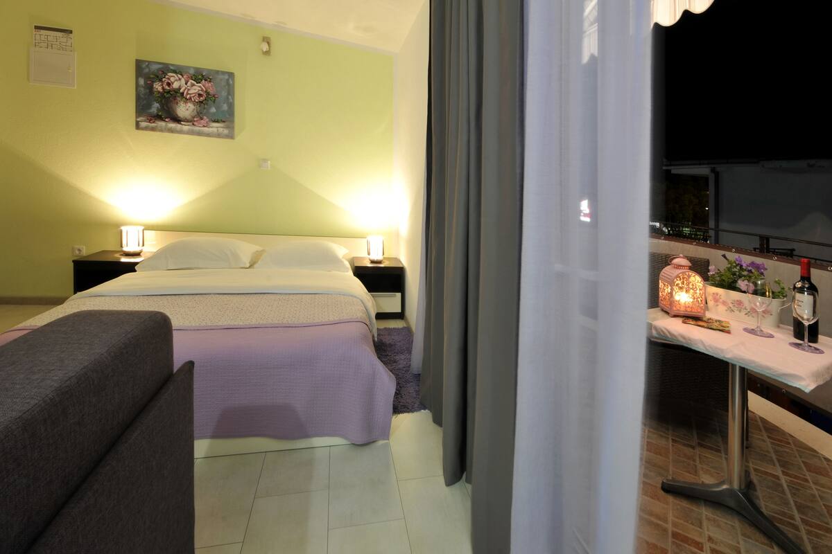 Hotelkamer met een bed, nachtkastjes, een lamp, een schilderij aan de muur en een balkon met een tafel en decoratieve objecten.