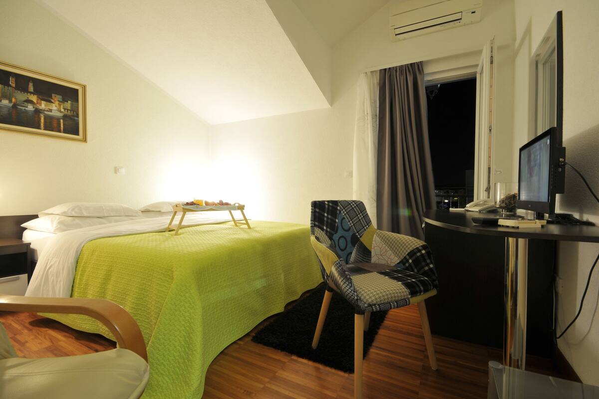Een hotelkamer met een bed, een bureau met een computer, een stoel en een schilderij aan de muur.
