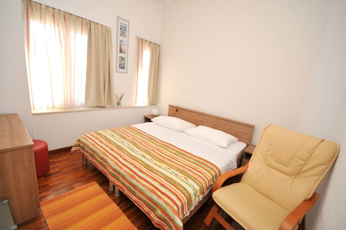 Een slaapkamer met een bed, een stoel, een bureau en een raam met gordijnen.