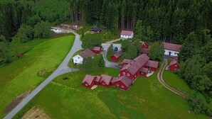 Vista aèria d'una zona rural amb diverses cases vermelles agrupades, envoltades per camps verds i un bosc dens.