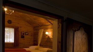 Habitació de cabana de fusta amb un llit, una finestra amb cortines i una làmpada penjada a la paret.