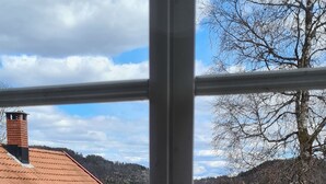 Edifici vermell amb teulada metàl·lica, zona pavimentada al davant i vista d'un paisatge amb turons per una finestra.