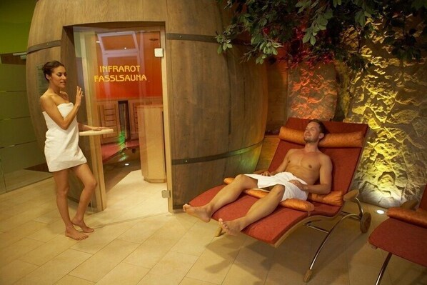 A spa area with a sauna, a woman in a towel, and a man relaxing in a chair. - Posthotel Thaller (Anger)