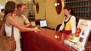 Een receptiebalie met een rode, beklede toonbank, een laptop en een tijdschriftrek met een 'THALLER' tijdschrift.