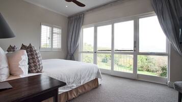A bedroom with a large bed, a ceiling fan, a desk, and a window with curtains.