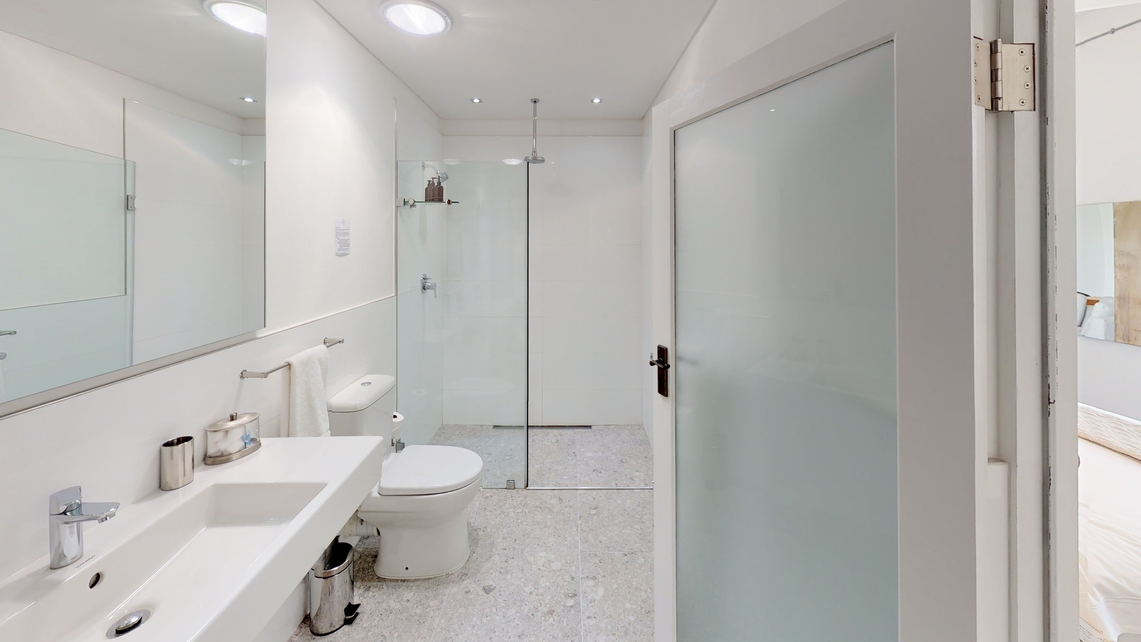 Een moderne badkamer met een douchecabine van glas, een witte wastafel met chroomaccenten en een toilet.