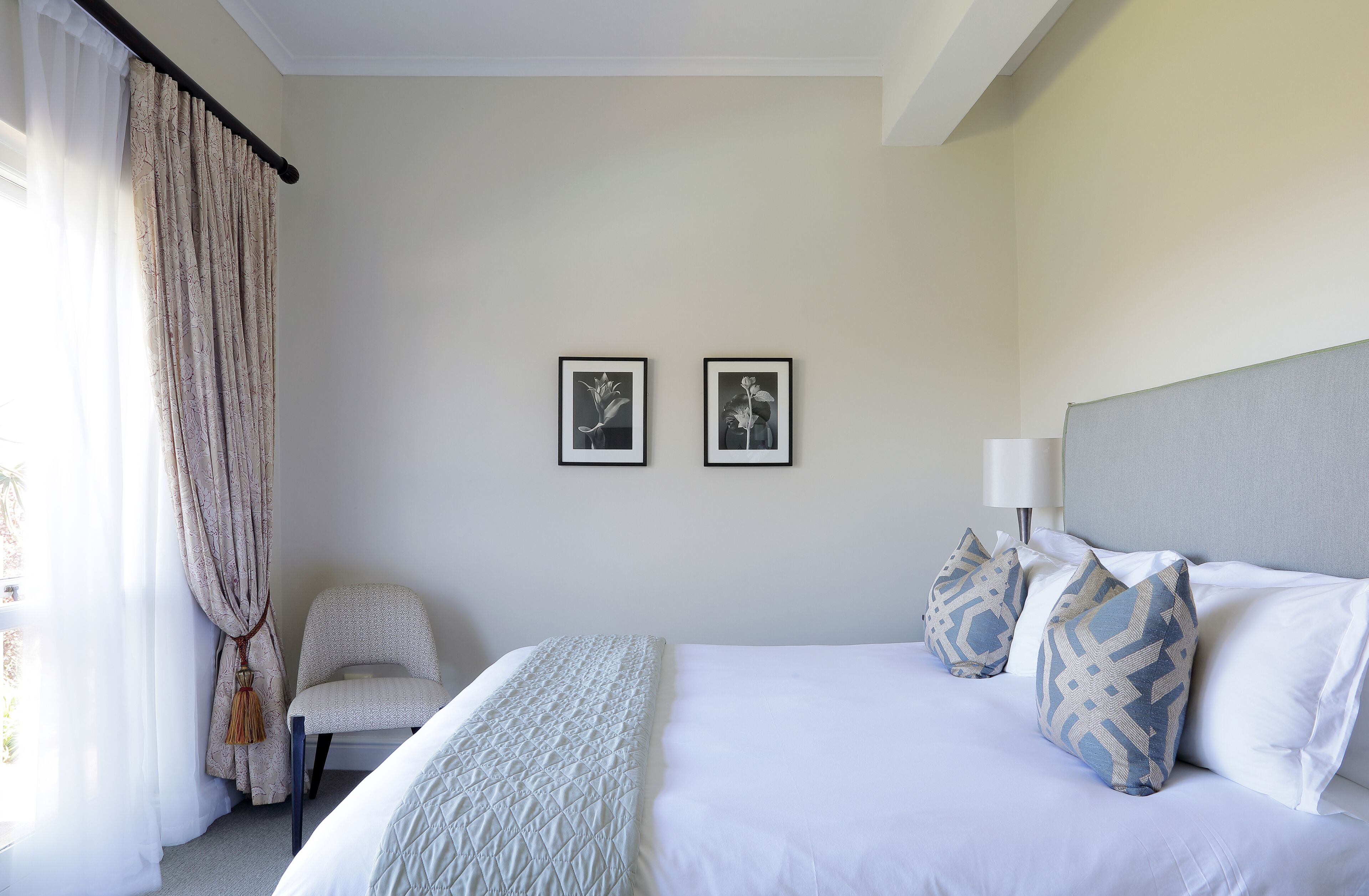 A neatly arranged bedroom with a bed, a chair, and two framed pictures on the wall.