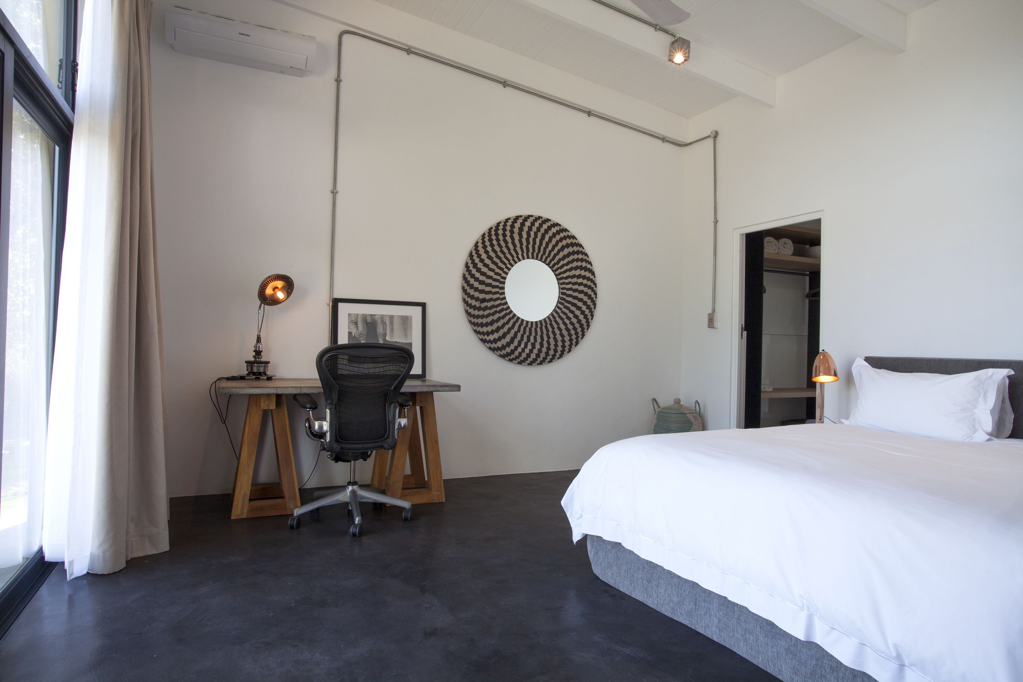 Una camera d'albergo con un letto grande, una scrivania con una sedia, uno specchio tondo e un armadio.