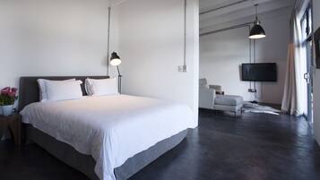 A modern bedroom with a large bed, bedside lamp, and a TV in the adjacent living area.