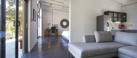 Una sala moderna con un sofá gris, una cafetera y una zona de cocina con armarios.